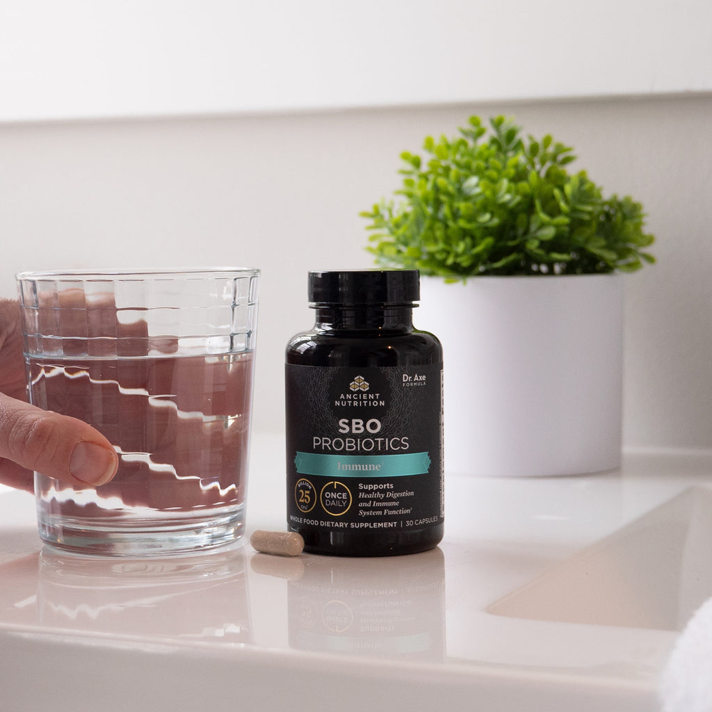person grabbing cup of water next to SBO Probiotics Immune Once Daily