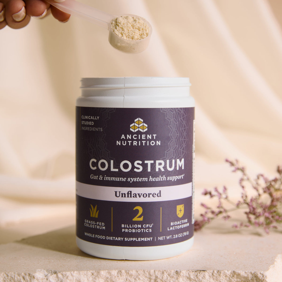 bottle of Colostrum Powder Unflavored (60 Servings) with a scoop of powder