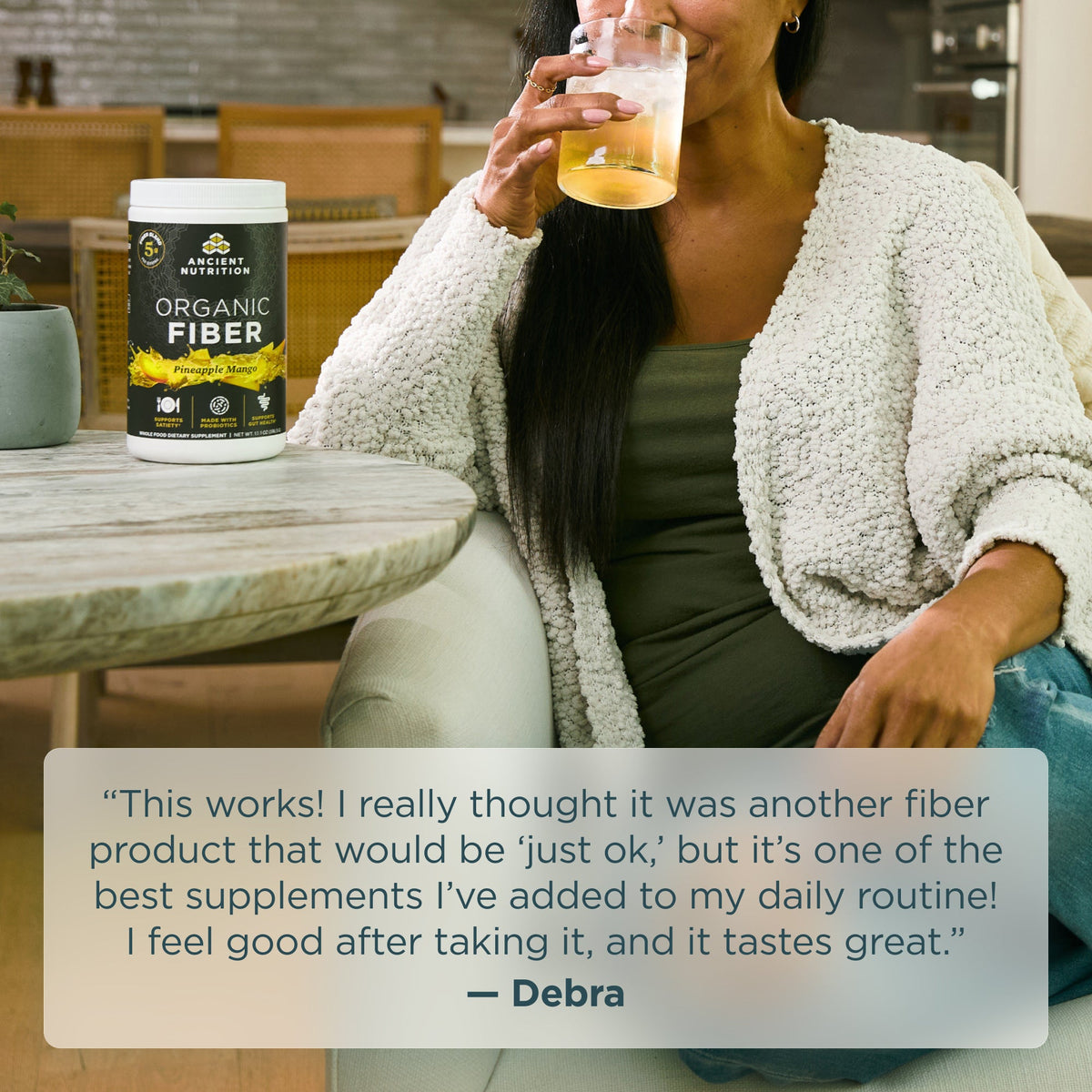 Woman drinking a beverage next to a container of Organic Fiber powder pineapple mango on a table