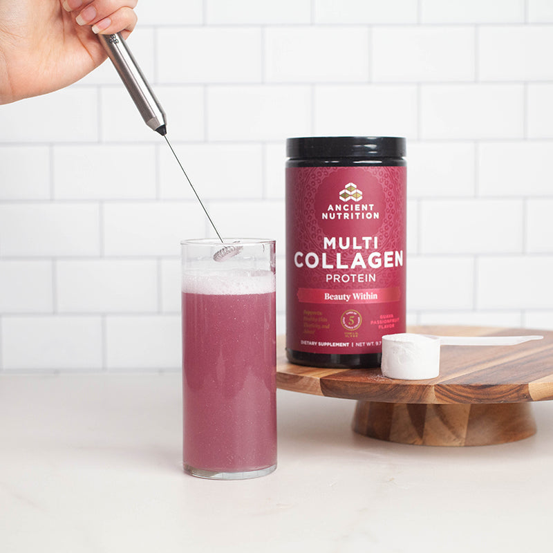 person using frother in a cup next to a bottle of collagen