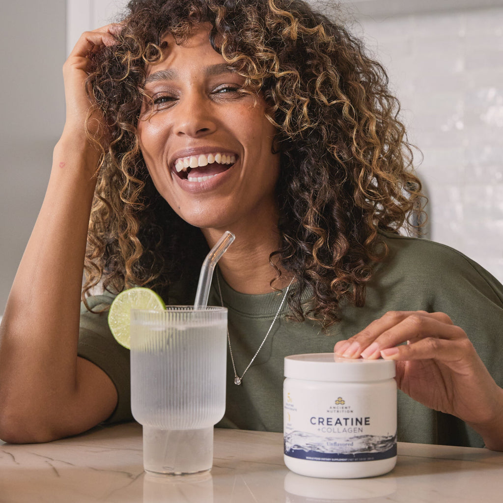Woman sitting at a table with a glass of water and a container labeled 'Creatine'.
