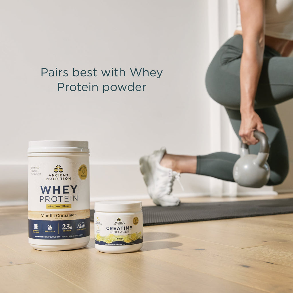 Whey protein powder container and creatine supplement on a wooden floor with a person exercising in the background.