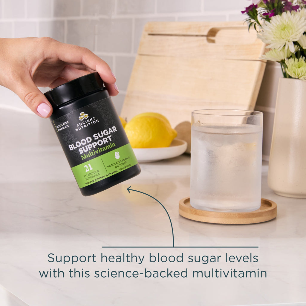 Hand holding a supplement bottle labeled 'Blood Sugar Support Multivitamin' on a kitchen counter.