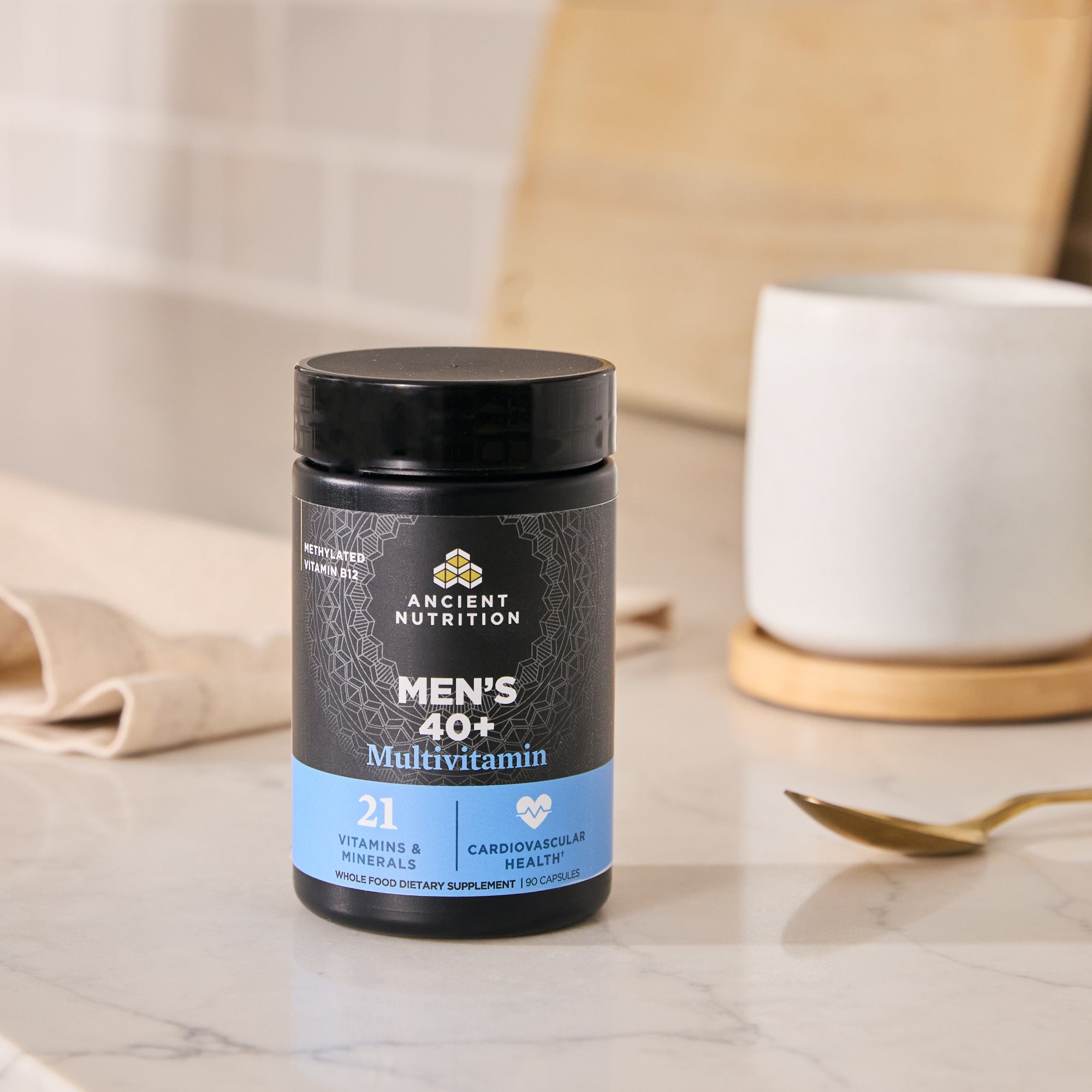 Ancient Multivitamin Men's 40+ Capsules bottle on a marble surfact with a cup and spoon in the background
