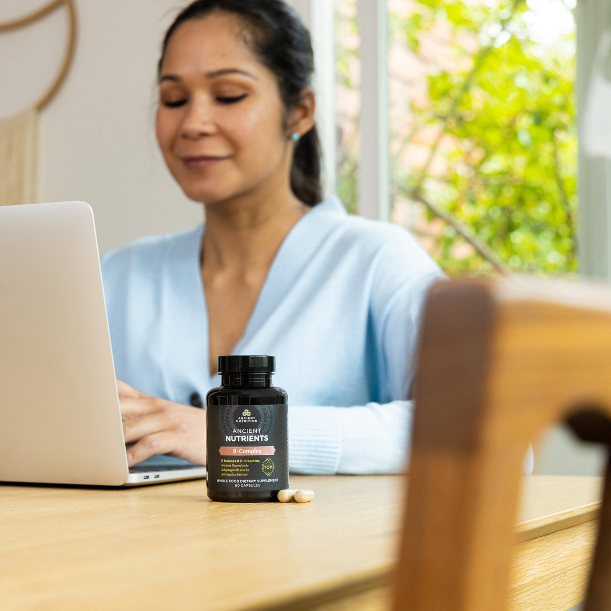 a women working on her computer with a bottle on Ancient Nutrients Vitamin B Complex Capsules (30 Servings) on her desk