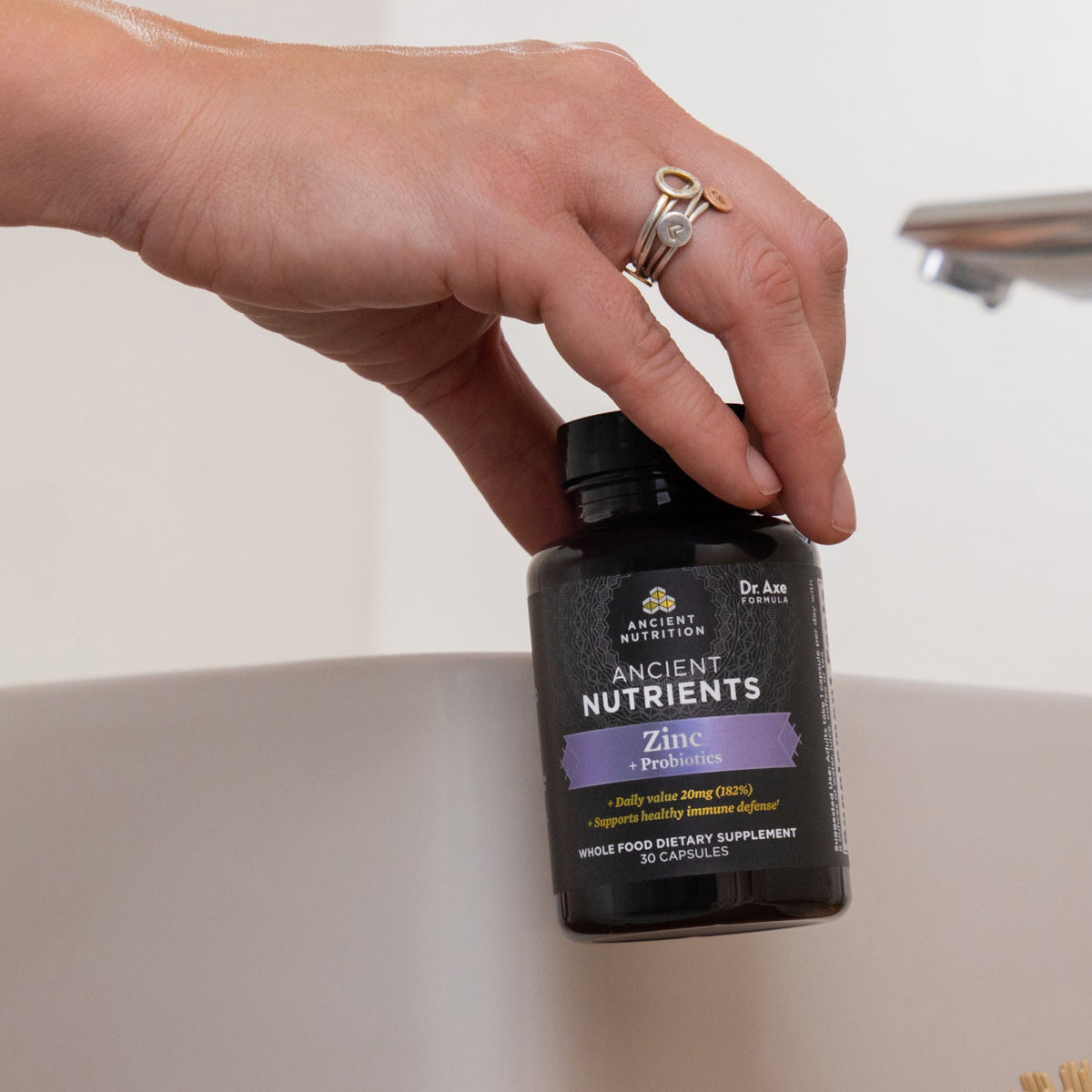 a woman holding a bottle of Ancient Nutrients Zinc + Probiotics Capsules (30 Servings)