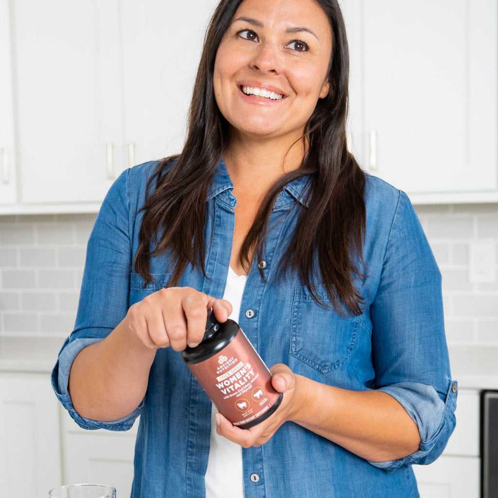 a woman holding a bottle of Women's Vitality Once Daily Tablets