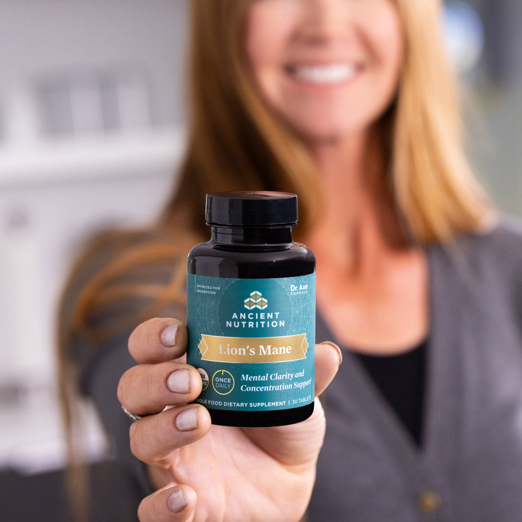 a woman holding a bottle of Lion's Mane Mental Clarity and Concentration Tablets on a counter