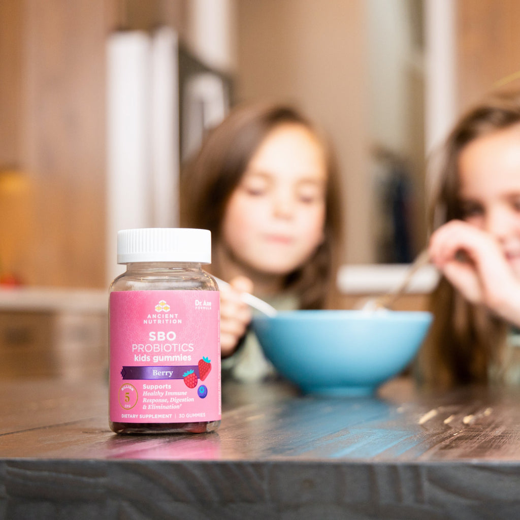a bottle of SBO Probiotics Kids Gummies Berry on a kitchen table with a bowl of cereal in the background