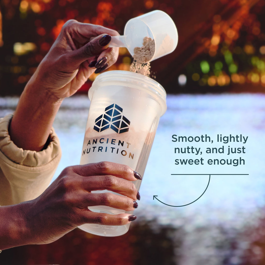 Person pouring powder into a Ancient Nutrition branded shaker bottle with a blurred background